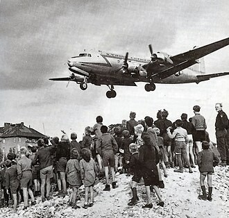 Children watching a transport aircraft approach Tempelhof during the Berlin Airlift.
