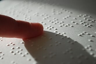 A reader’s finger passing over raised Braille characters.